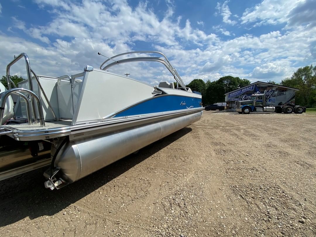A white and blue pontoon boat is parked in a gravel lot.