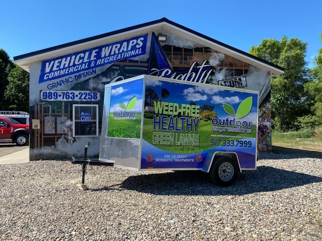 A trailer is parked in front of a building that says vehicle wraps.