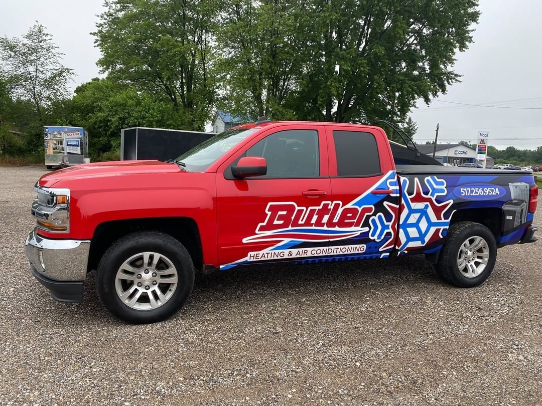 A red truck is parked in a gravel lot.