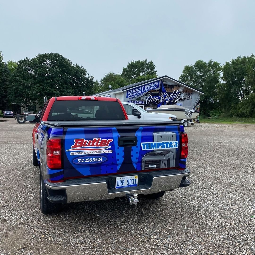 A blue and red truck is parked in a gravel lot in front of a building.