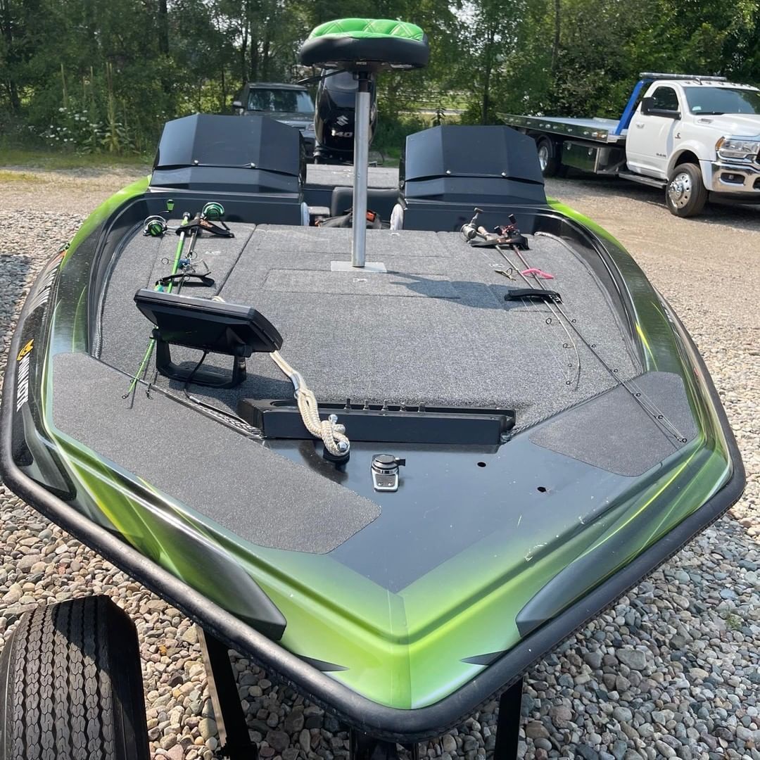 A green and black boat is parked in a gravel lot.