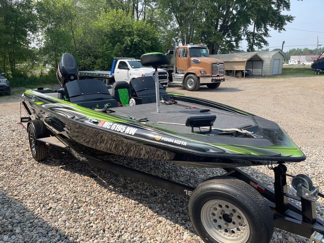 A fishing boat is parked on a trailer in a gravel lot.