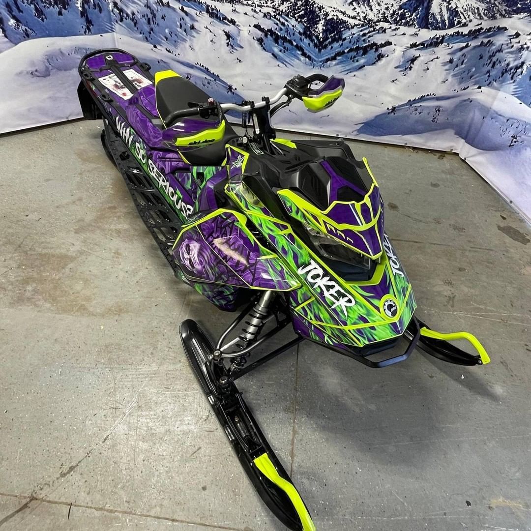 A green and purple snowmobile is parked in a garage.