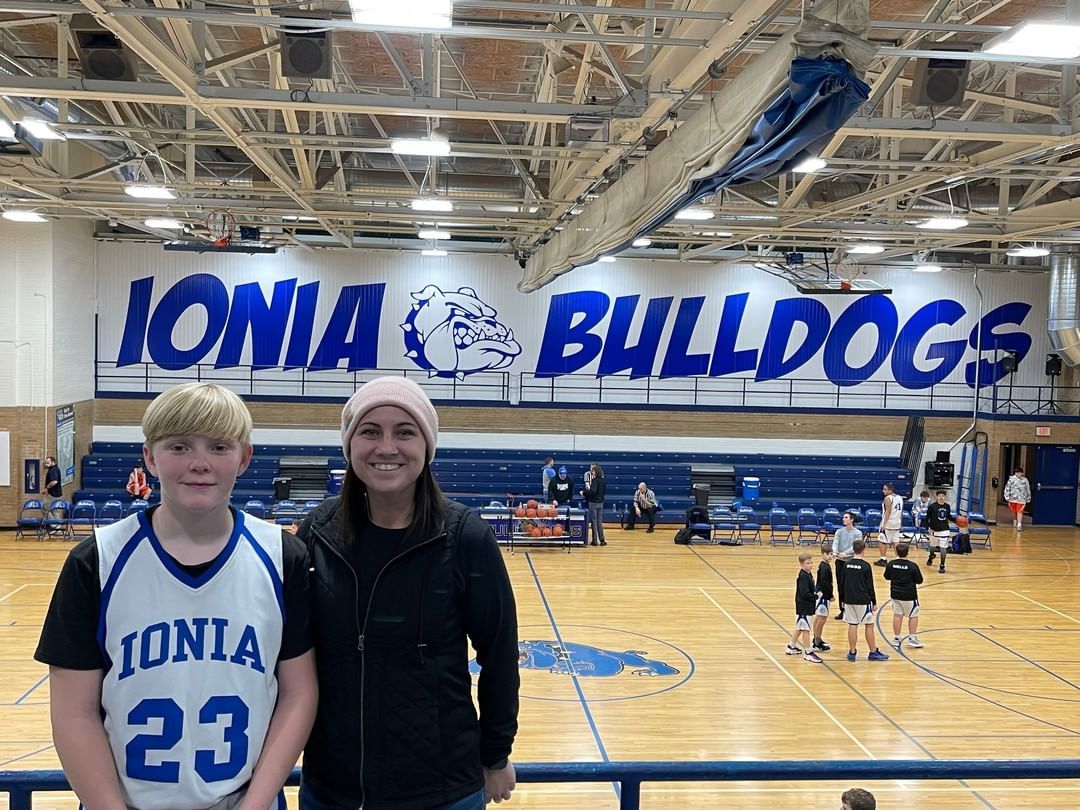 A woman and a boy are standing in front of a basketball court.
