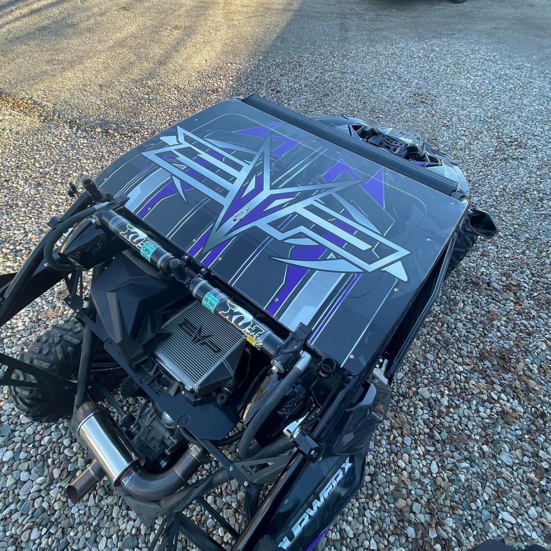 A black and purple atv is parked in a gravel lot.