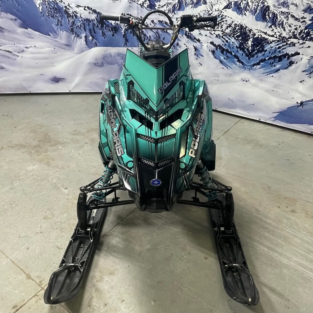 A green snowmobile is parked in front of a snowy mountain.