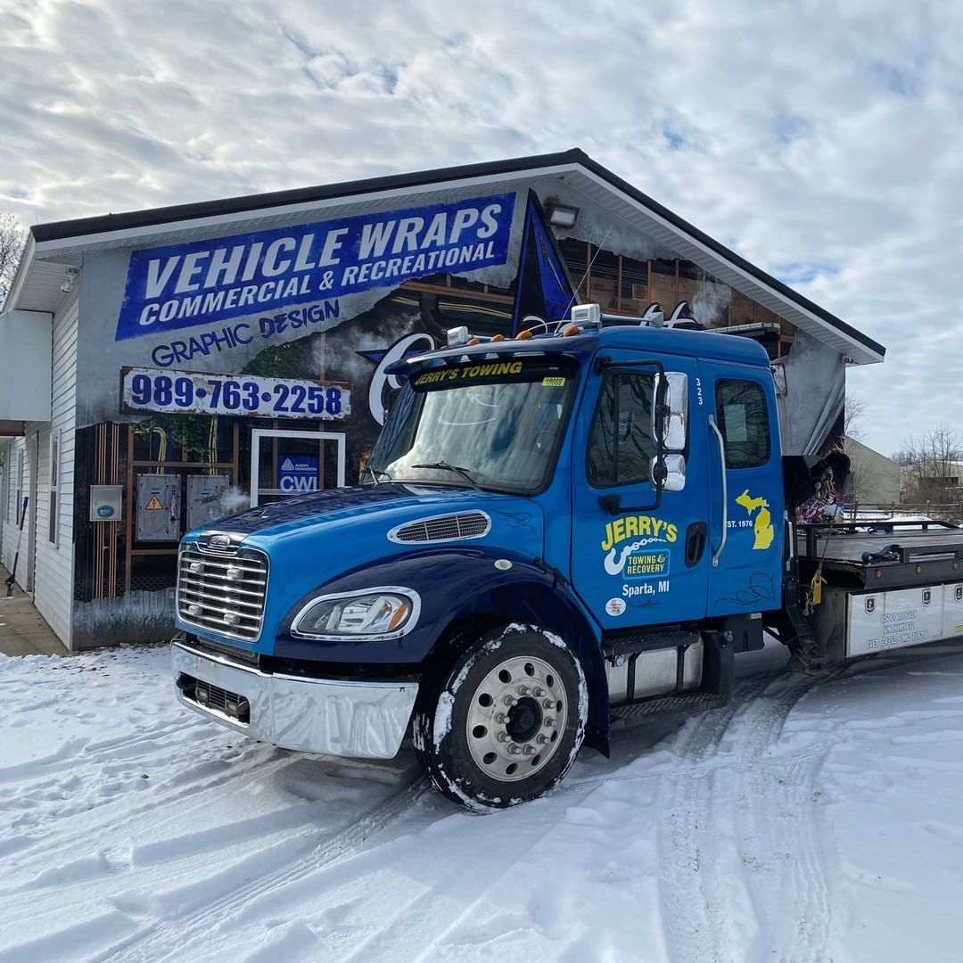 A blue truck is parked in the snow in front of a building.