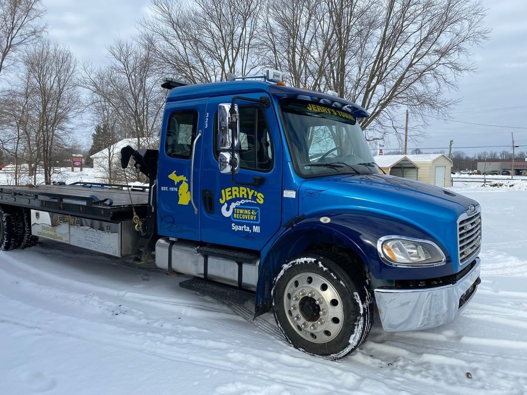 A blue tow truck is parked in the snow.