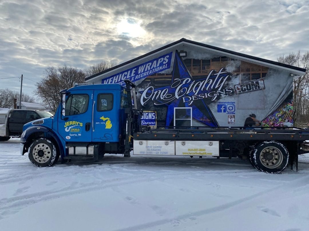 A blue tow truck is parked in the snow in front of a building.