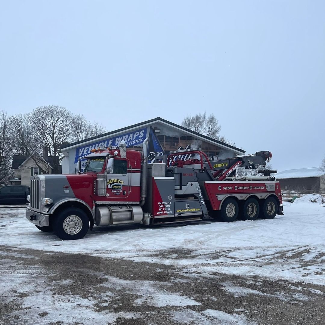 A red and gray tow truck is parked in the snow in front of a building.