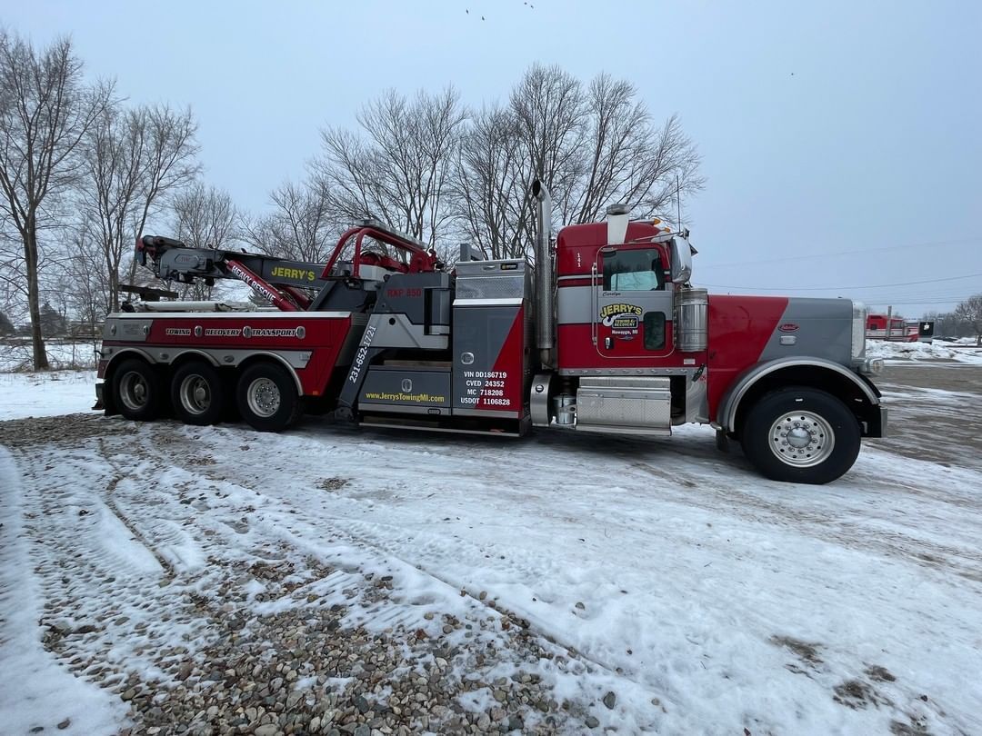 A red and gray tow truck is parked in the snow.