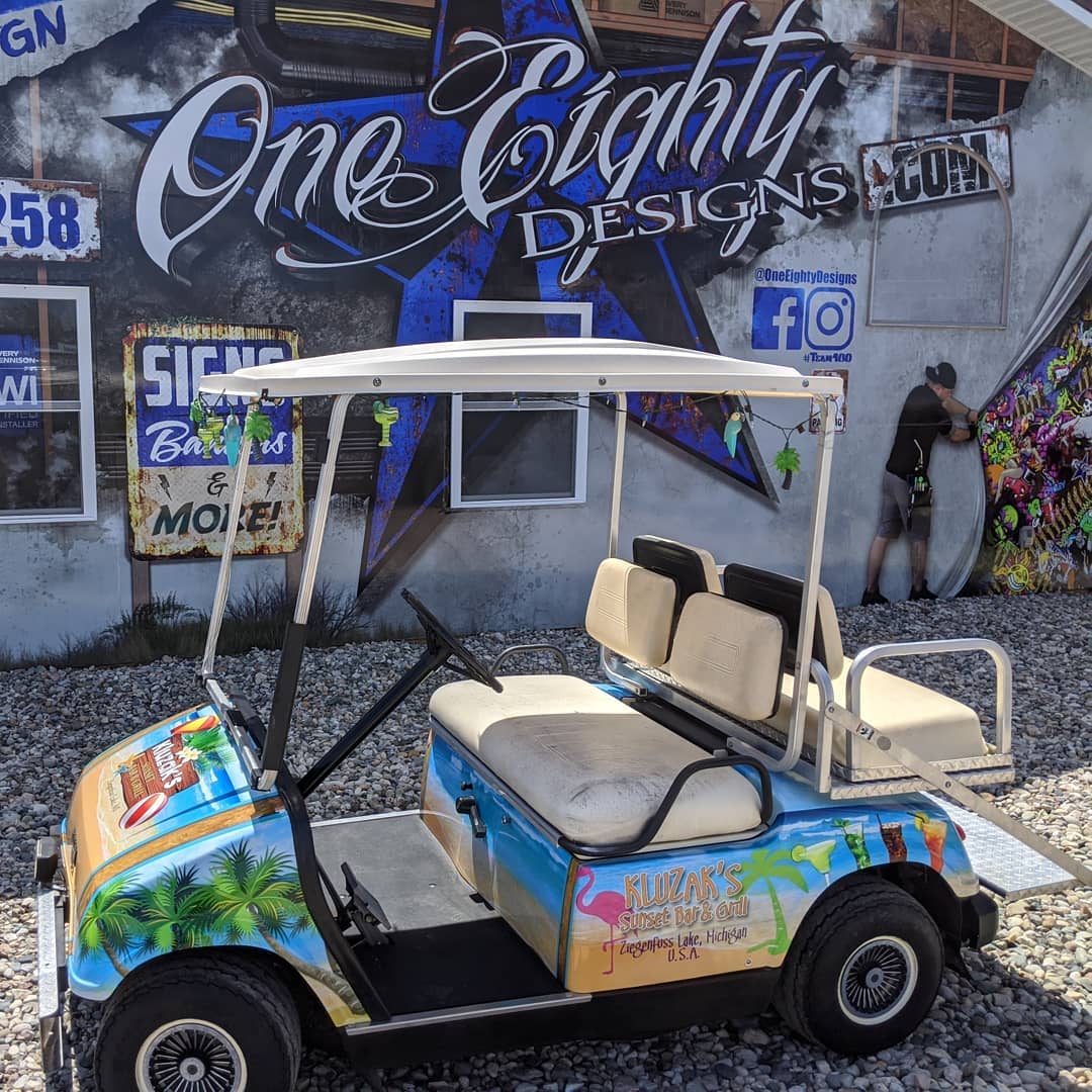 A golf cart is parked in front of a building that says one eighty designs