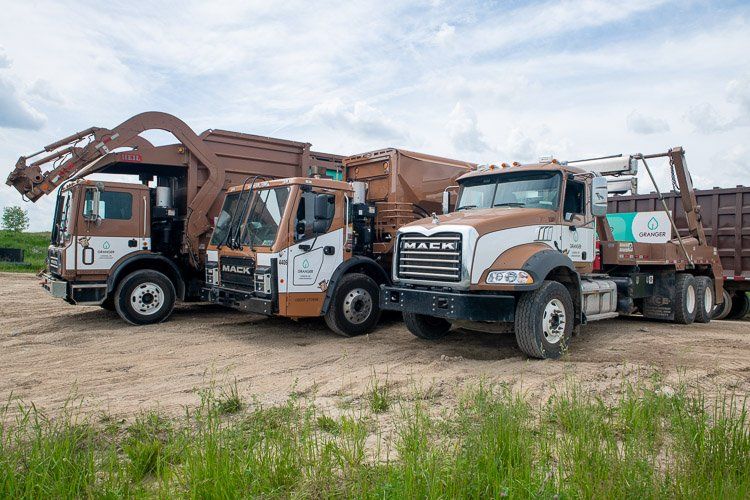 Three garbage trucks are parked next to each other in a dirt field.