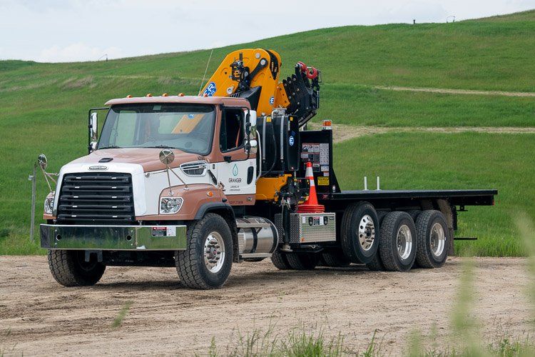 A flatbed truck with a crane on the back is parked in a dirt field.