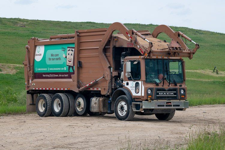 A garbage truck is driving down a dirt road