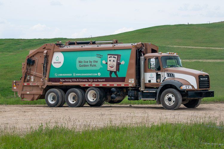 A garbage truck is driving down a dirt road.