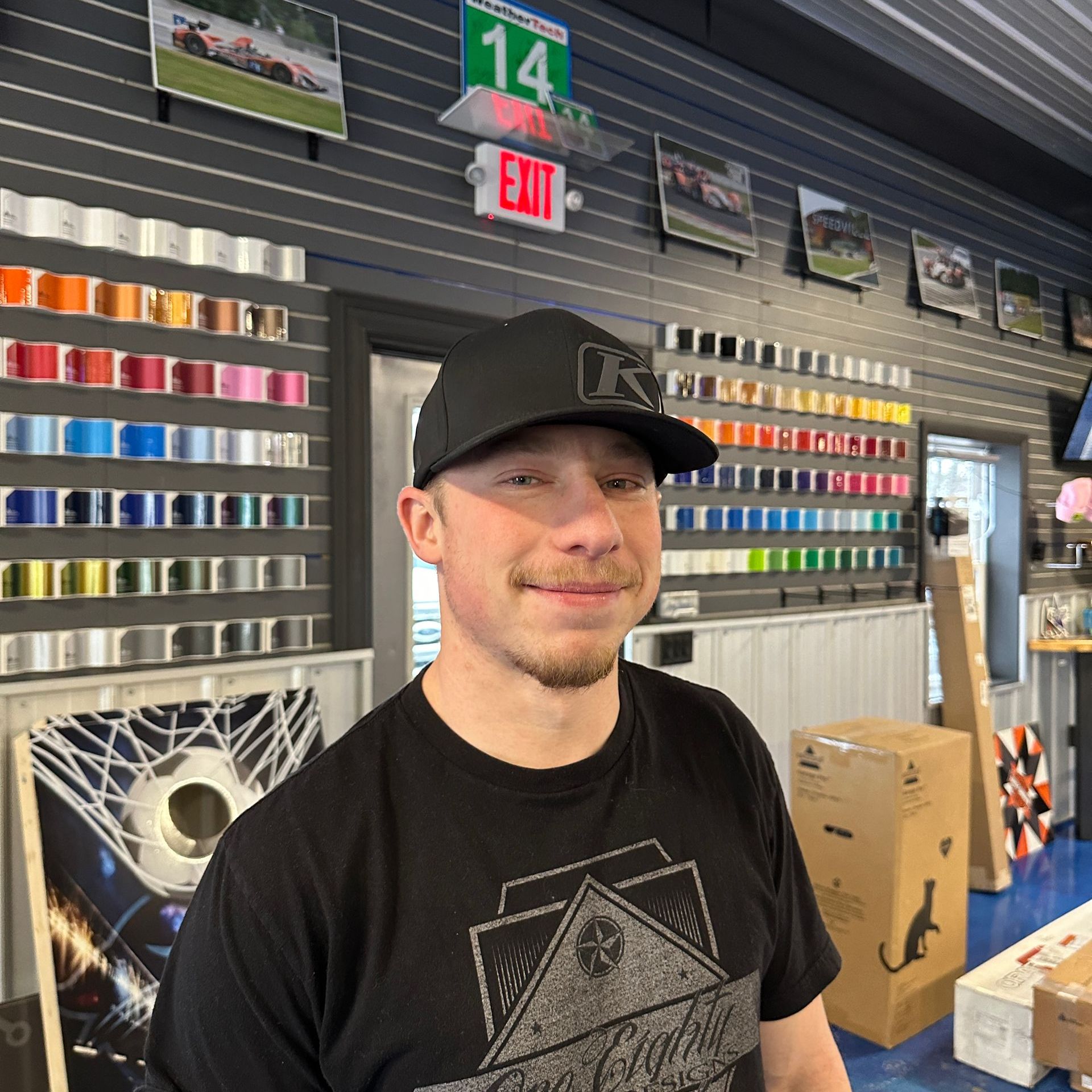 A man wearing a black hat and a black shirt is standing in front of an exit sign
