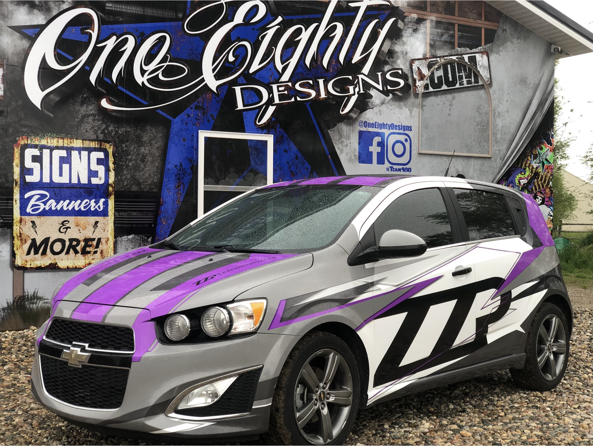 A gray and purple car is parked in front of a building.