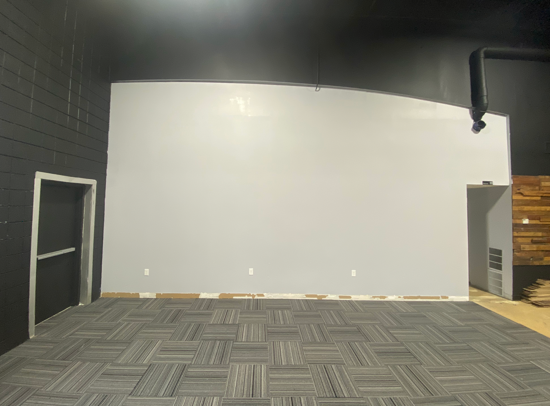 An empty room with a carpeted floor and a white wall.