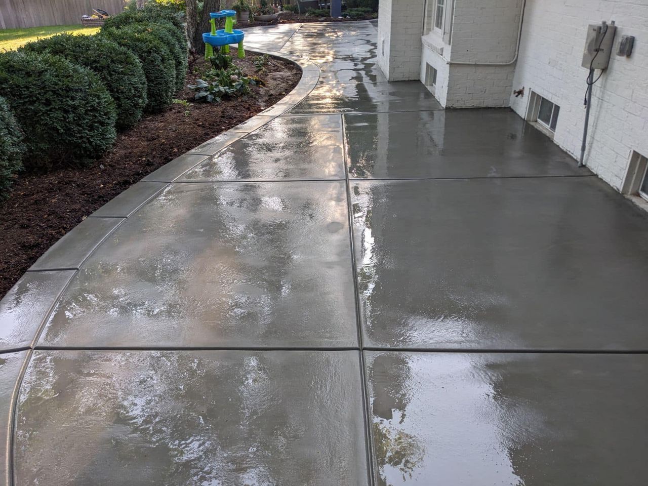A concrete walkway leading to a house with a blue chair in the background.