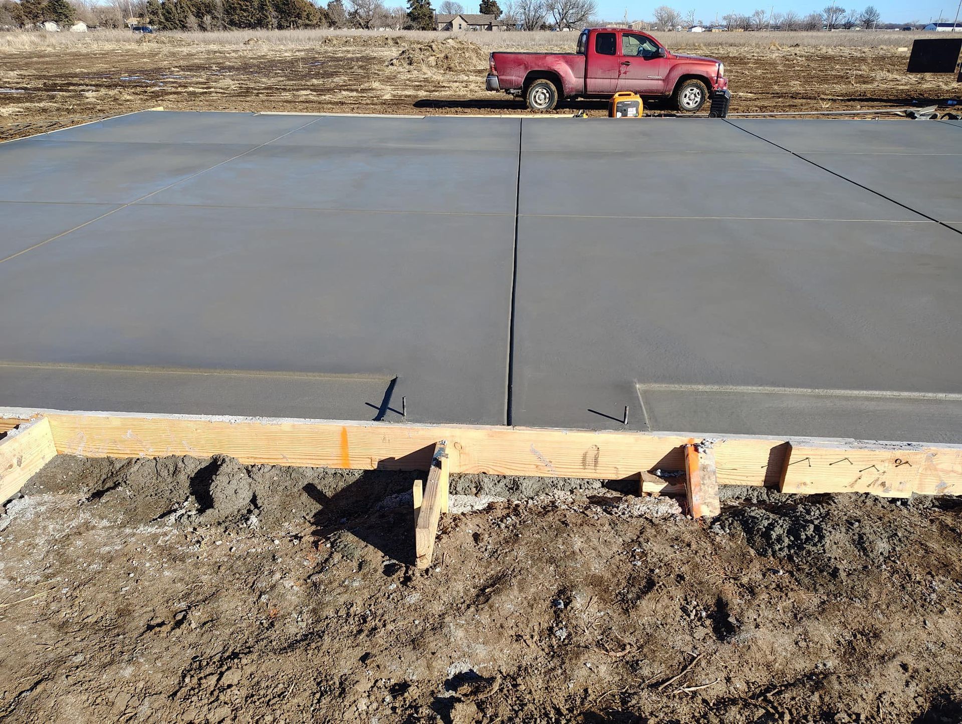 A red truck is parked on the side of a concrete driveway.