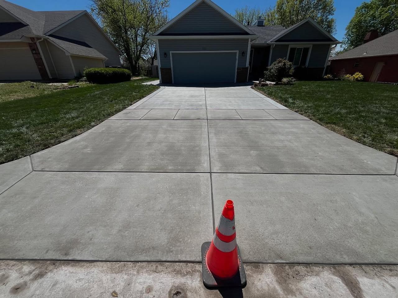 A concrete driveway with a traffic cone in front of a house.