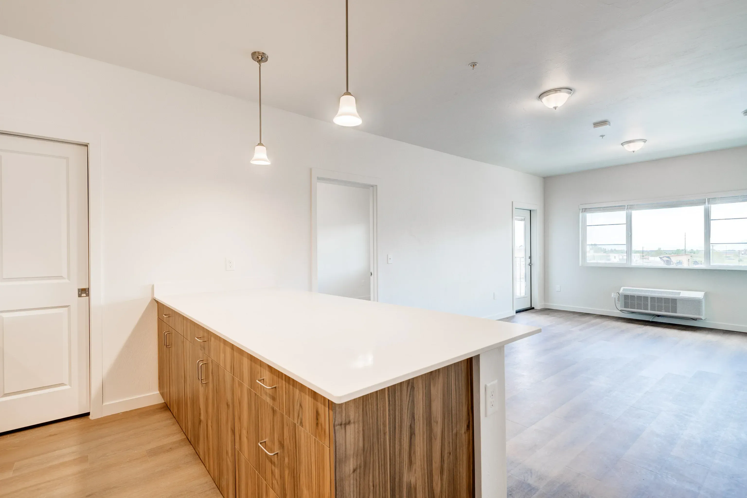 Open-concept kitchen with a white island and wood cabinets, adjacent living area with large window.