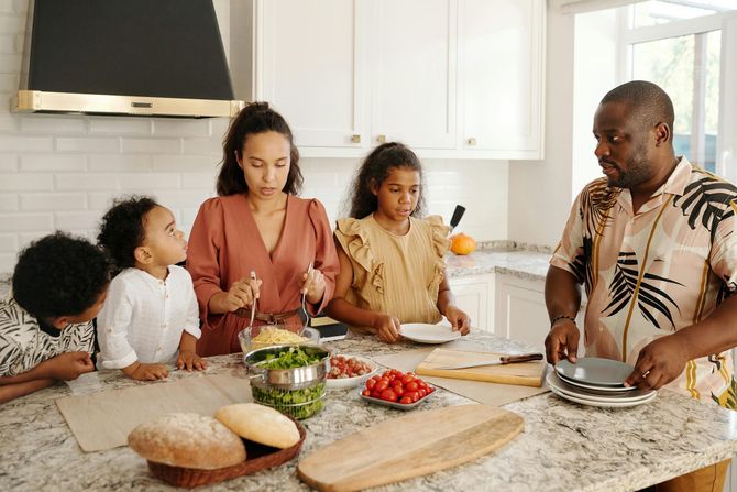 Family preparing food together in a bright kitchen around a countertop with vegetables and bread