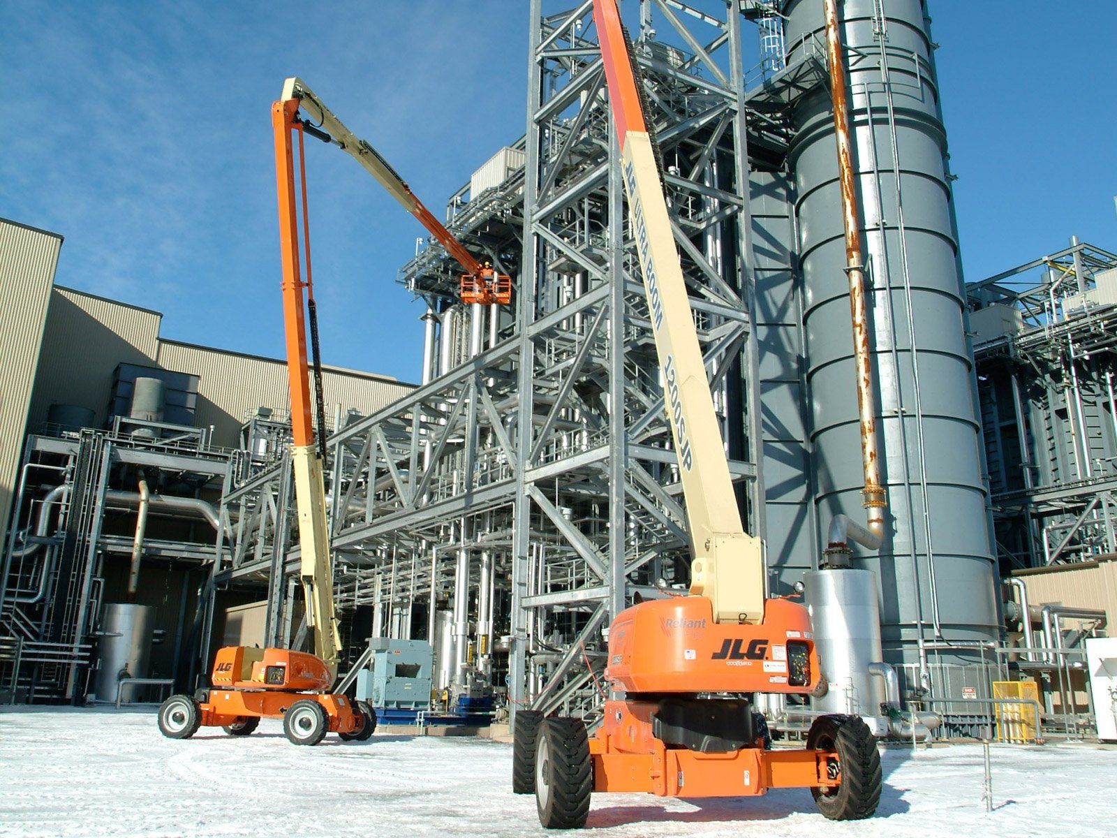 Two orange jlg lifts are parked in front of a large building