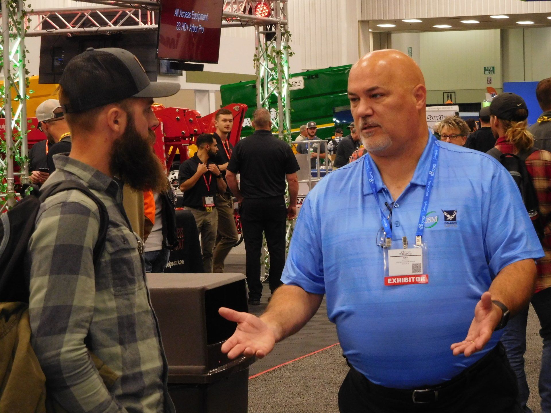 A man in a blue shirt is talking to another man in a plaid shirt.