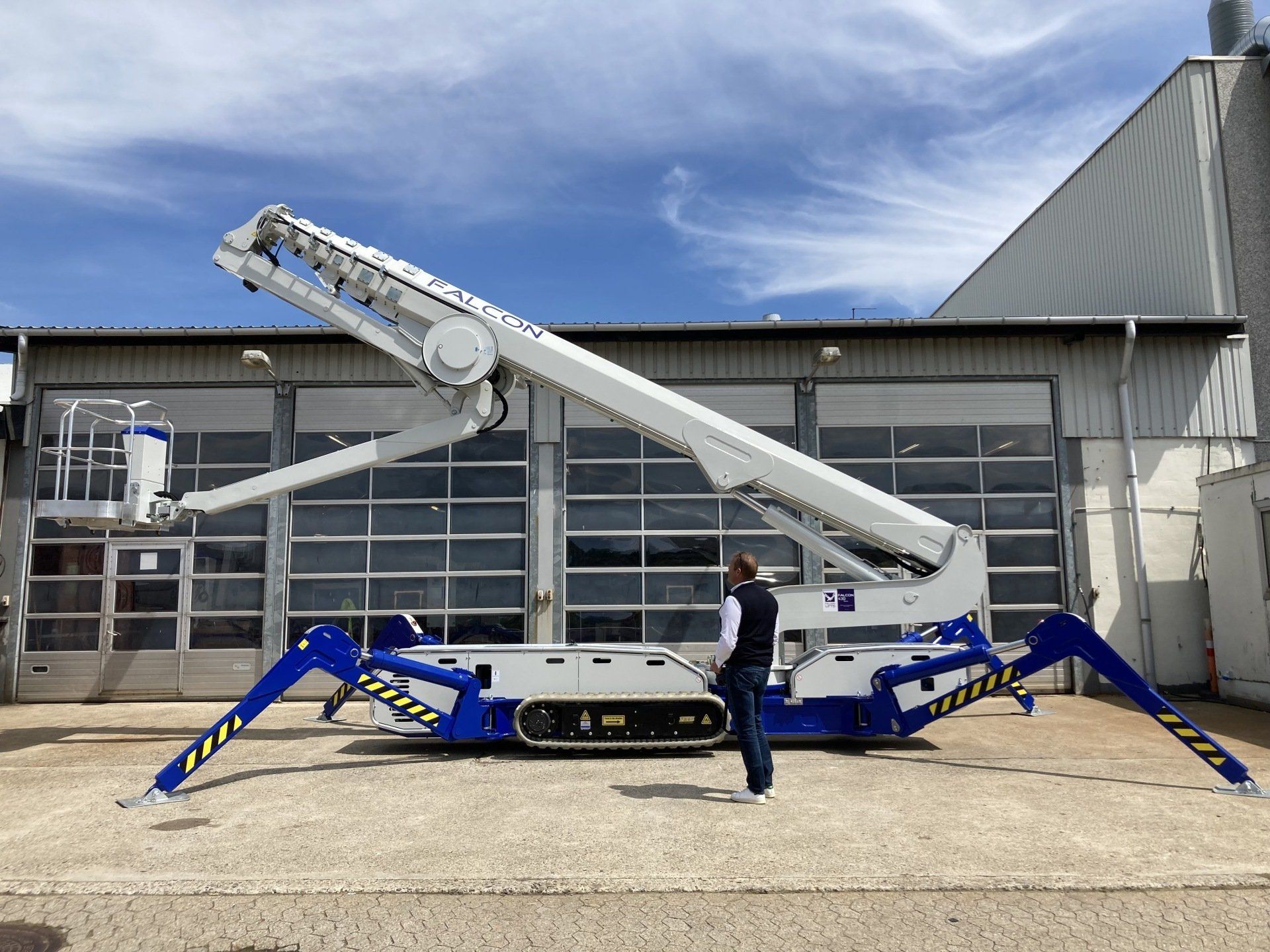 A man is standing next to a spider lift in front of a building.