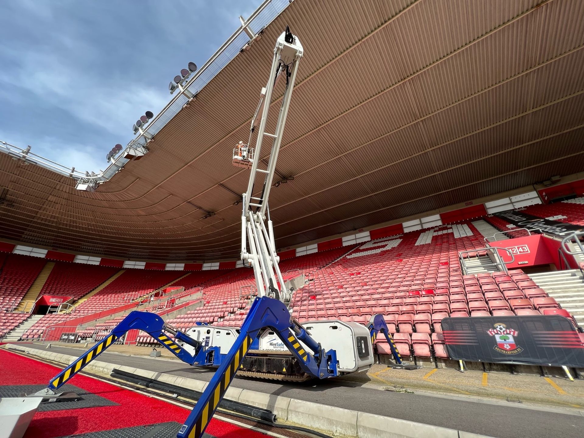 Blue and white spider lift aerial work platform on stadium job site under construction