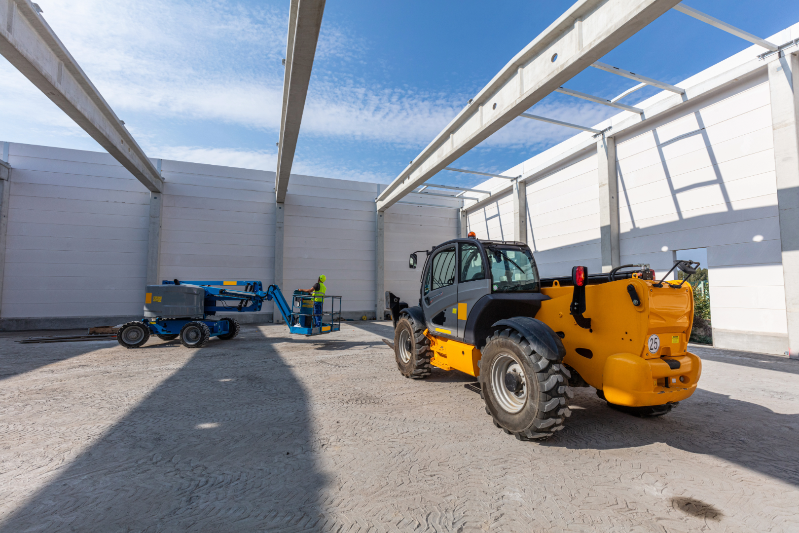 Dieci telehandler and Genie boom lift on warehouse job site with steel framing, concrete floor, and construction crew
