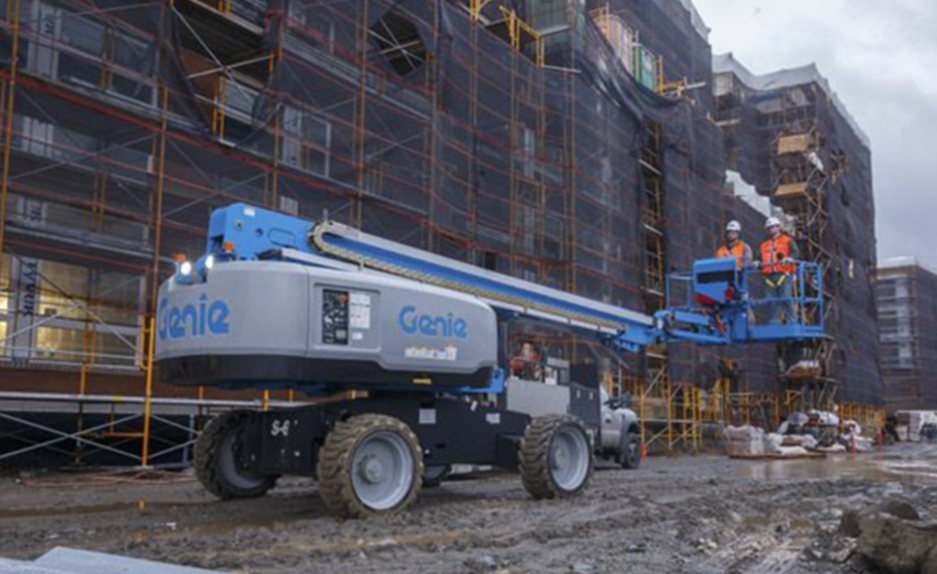 A genie lift is parked in front of a building under construction.