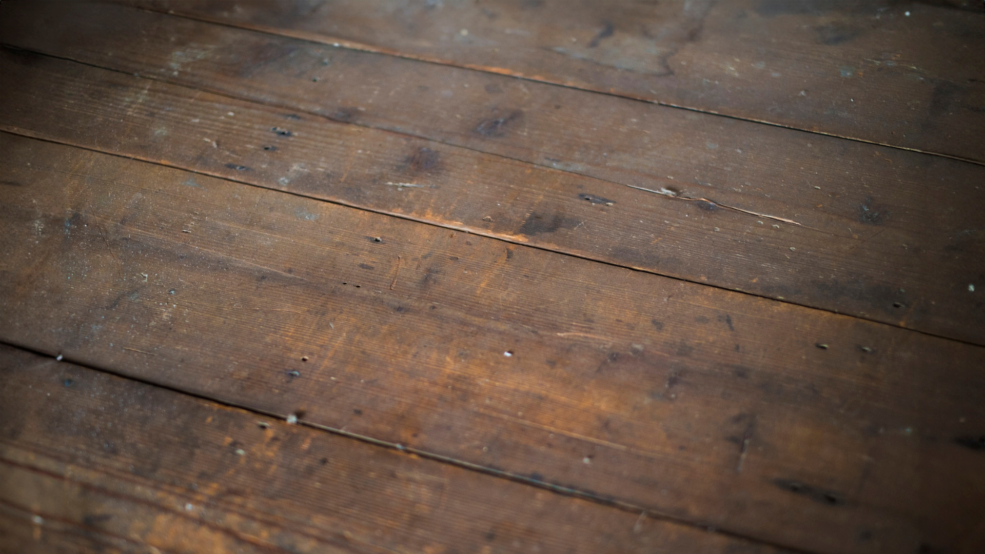 Close-up of weathered, dark brown wooden floor planks with visible grain and gaps between boards.