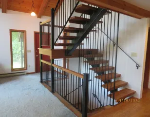 Interior view of a wooden staircase with black railings in a bright room with white walls and carpeted floor