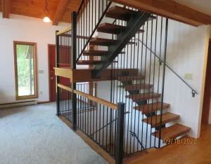 Interior view of a wooden staircase with black railings in a bright room with white walls and carpeted floor