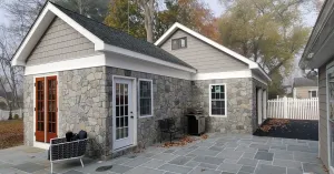 Stone house with white trim and front patio, showing a small entryway and paved courtyard