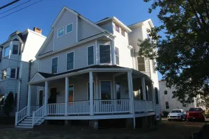 White Victorian-style house with wraparound porch and blue shutters, viewed from the front yard