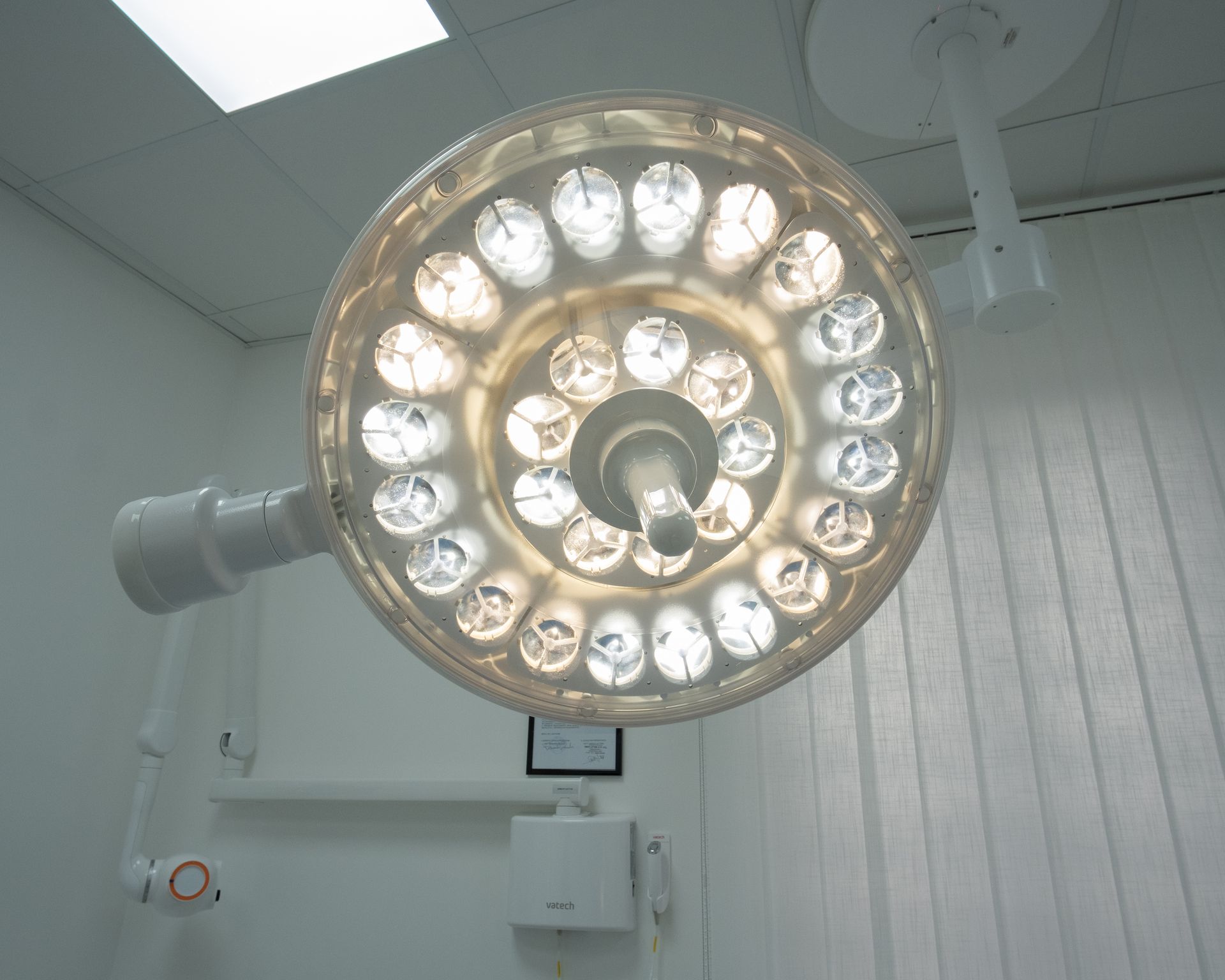 Una luminosa lampada chirurgica a soffitto, installata in una sala operatoria, illumina lo sfondo di pareti bianche.