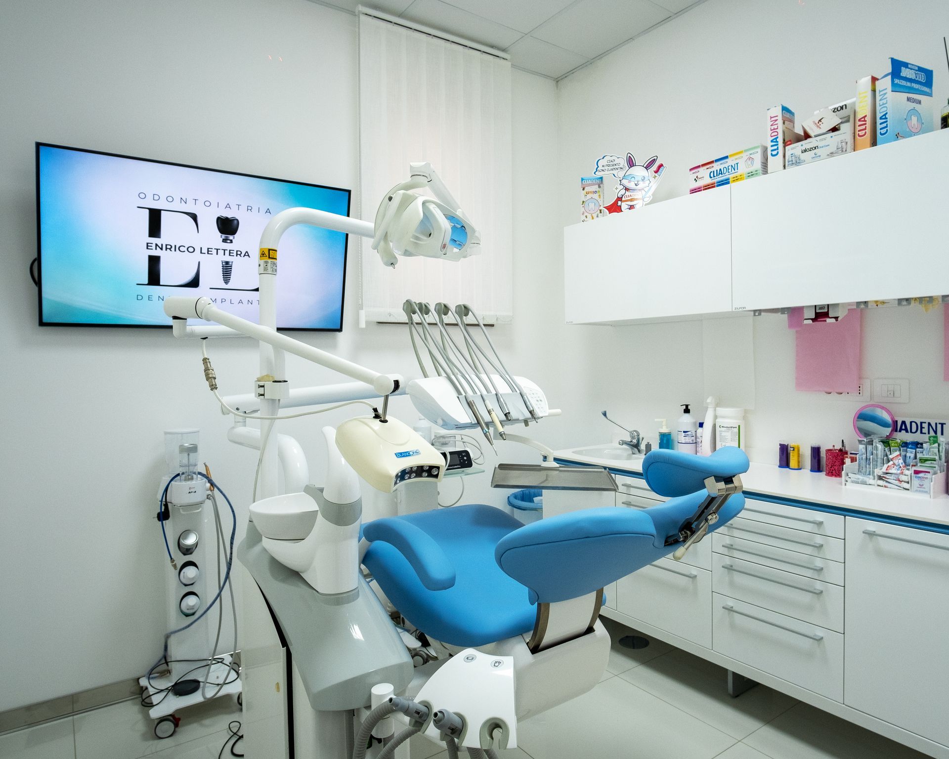 Clinica odontoiatrica moderna con poltrona da dentista blu, attrezzature e armadietti bianchi in una stanza luminosa.