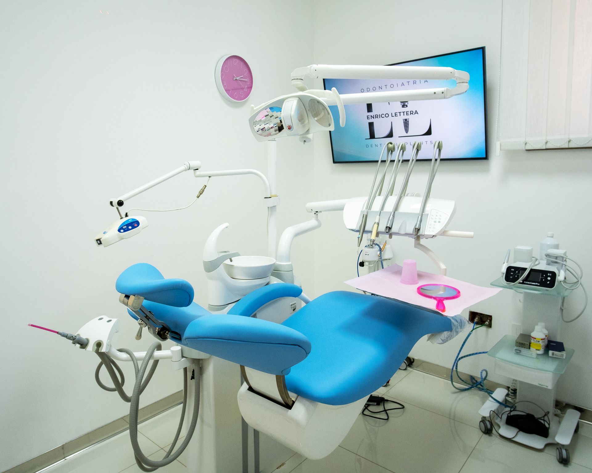 Clinica odontoiatrica moderna con poltrona blu, lampada a soffitto e strumenti in una stanza bianca e pulita.