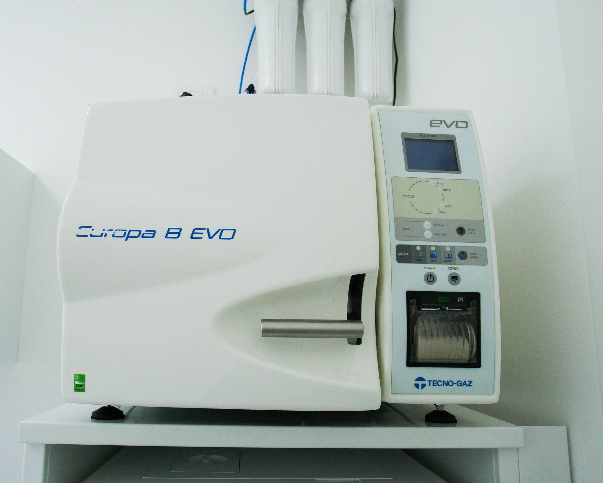 Sterilizzatore da banco in autoclave bianca con pannello di controllo e piccolo display su ripiano.