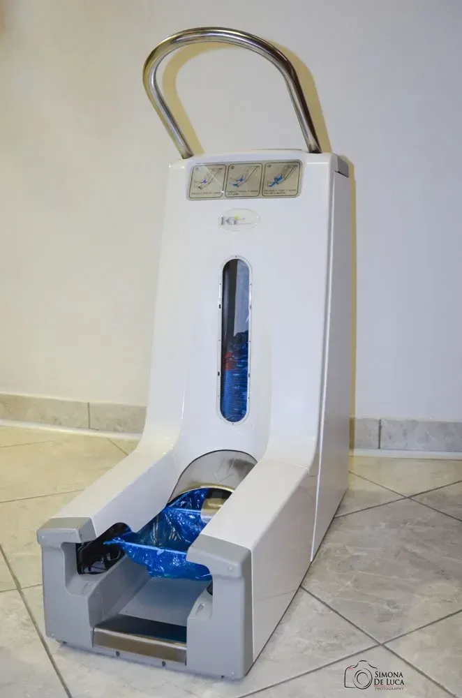 Dispenser di copriscarpe in schiuma bianca con coperchi blu, posizionato su un pavimento piastrellato.