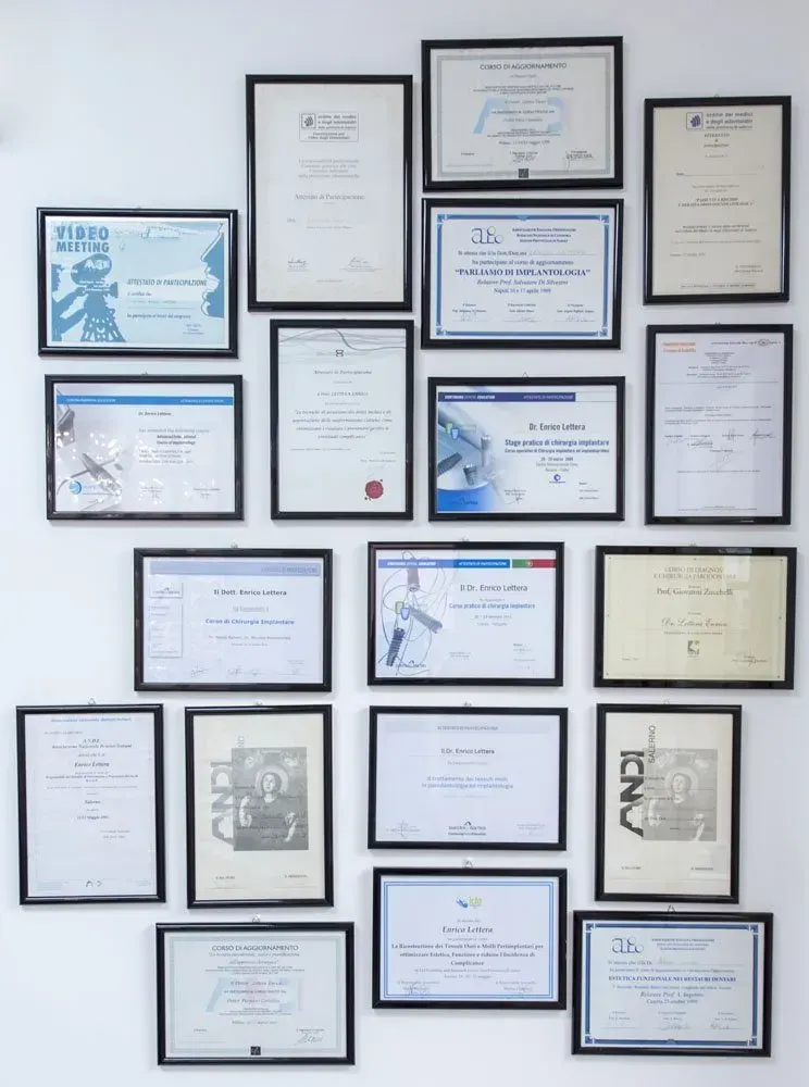 Parete di certificati e diplomi incorniciati in cornici nere, bianche e blu su una parete chiara
