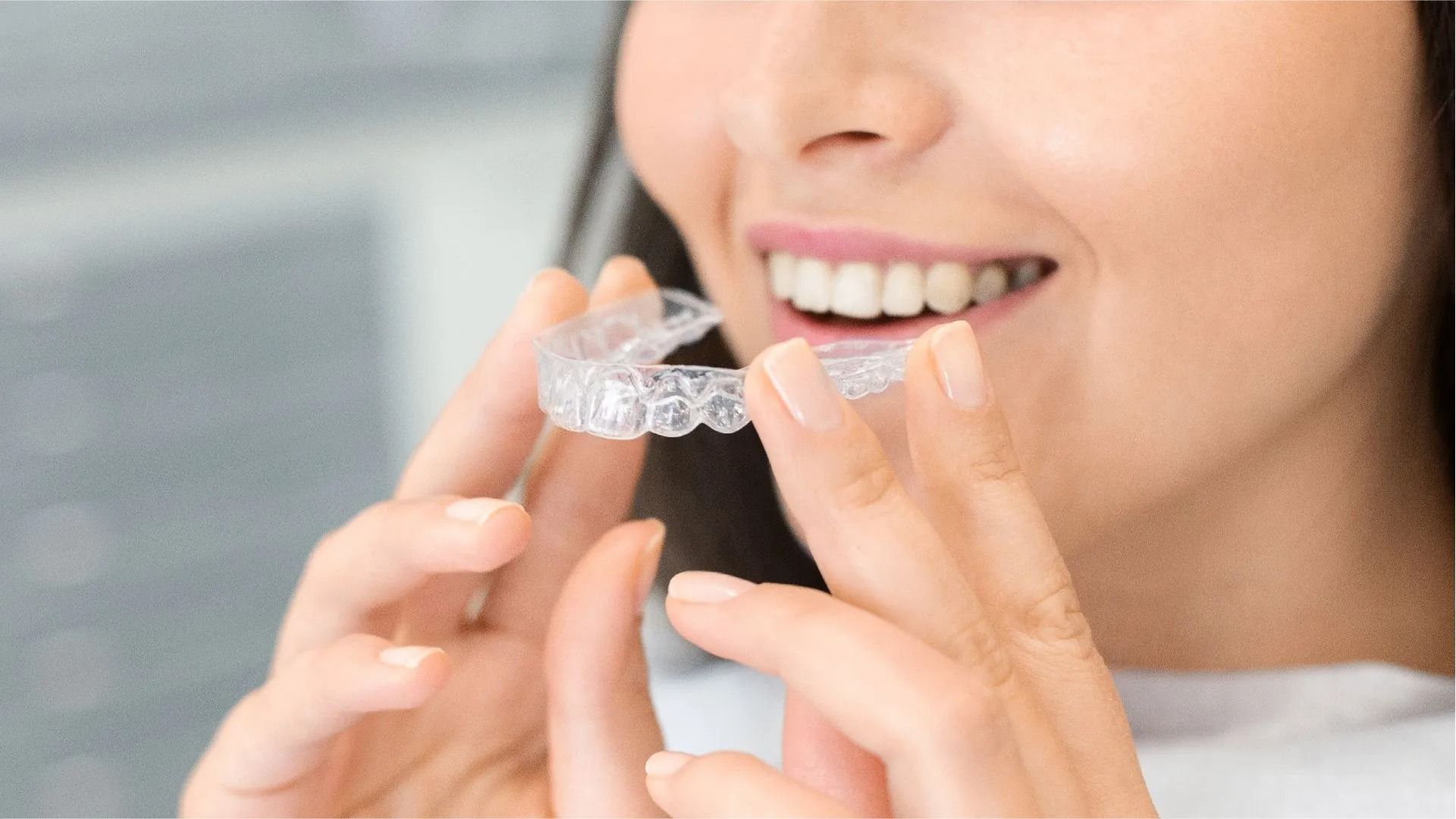 Una persona sorride mentre tiene vicino alla bocca un allineatore dentale trasparente.
