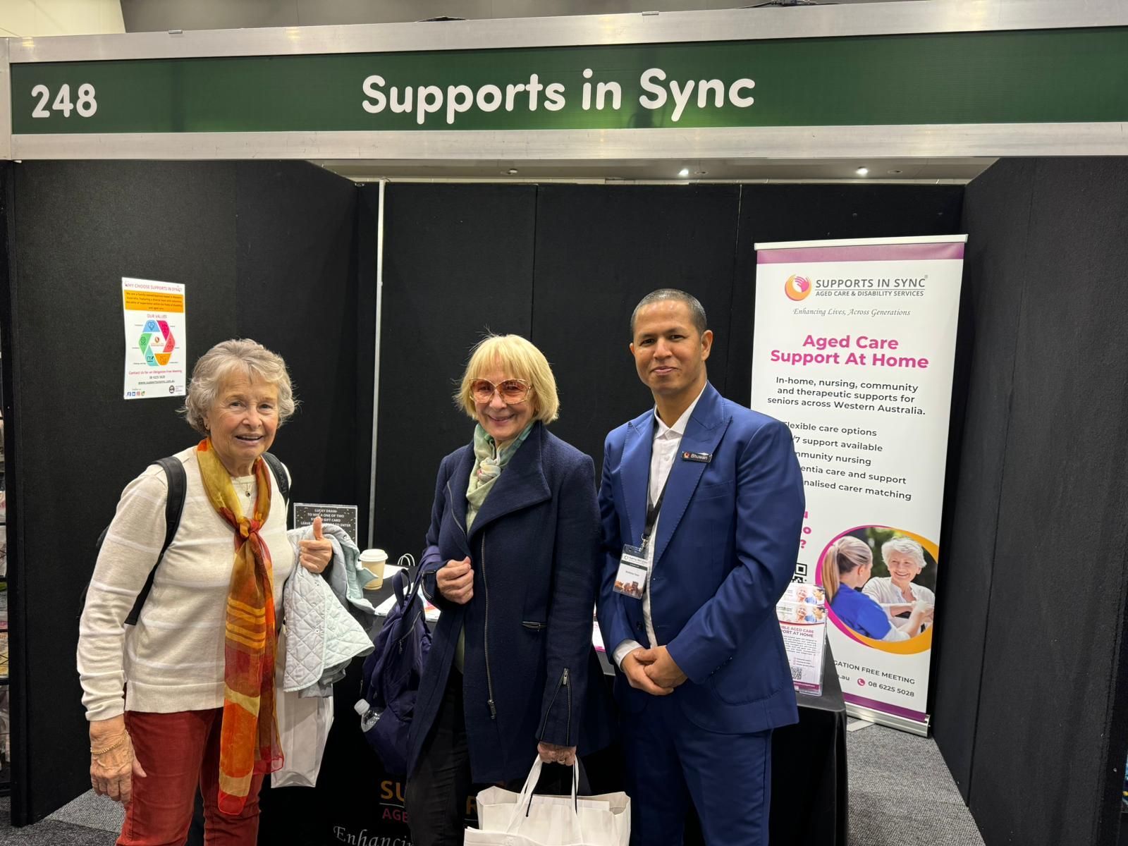 Three people are standing in front of a sign that says `` supports in sync ''.