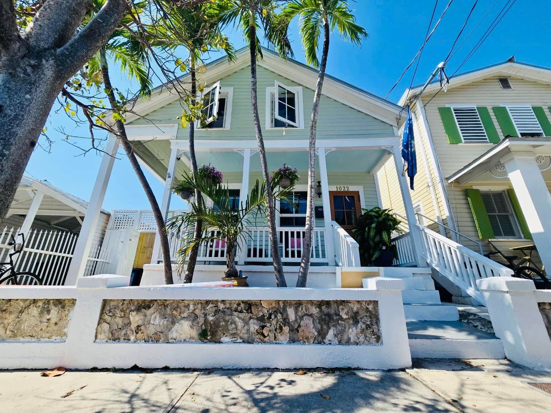 A house with a porch and stairs is surrounded by palm trees.
