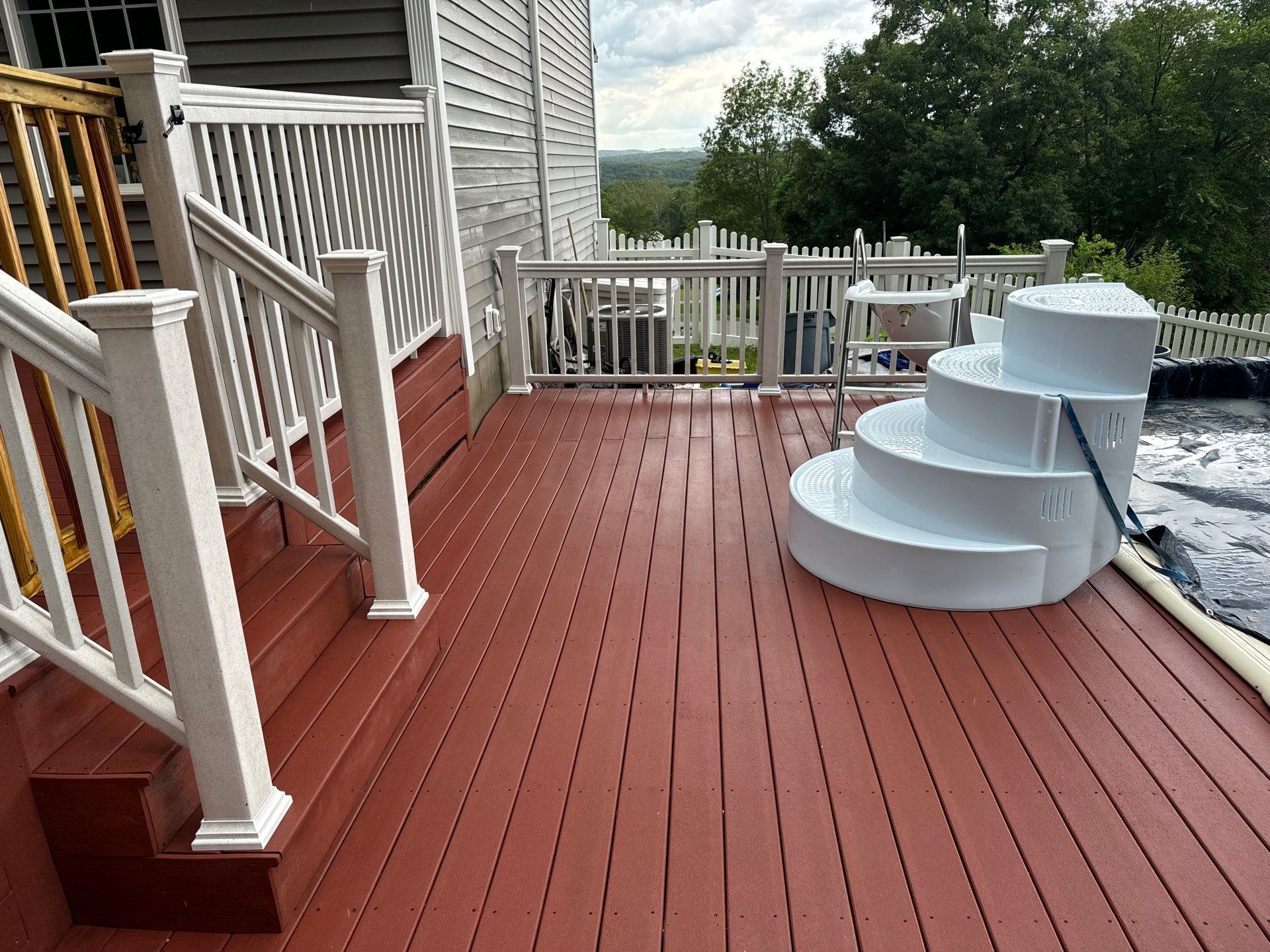 Red wooden deck with white railing; stairs lead to a pool.