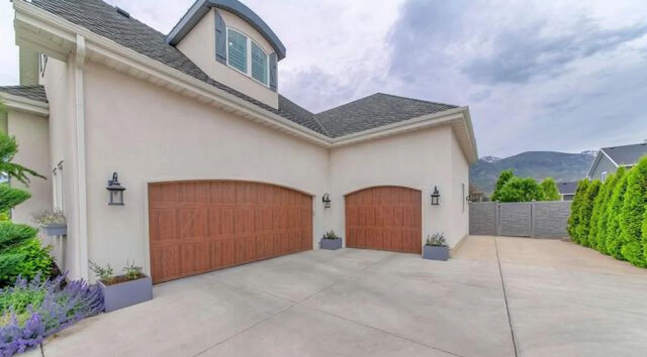 Suburban house exterior with two wooden garage doors, a wide driveway, and a side hedge-lined wall